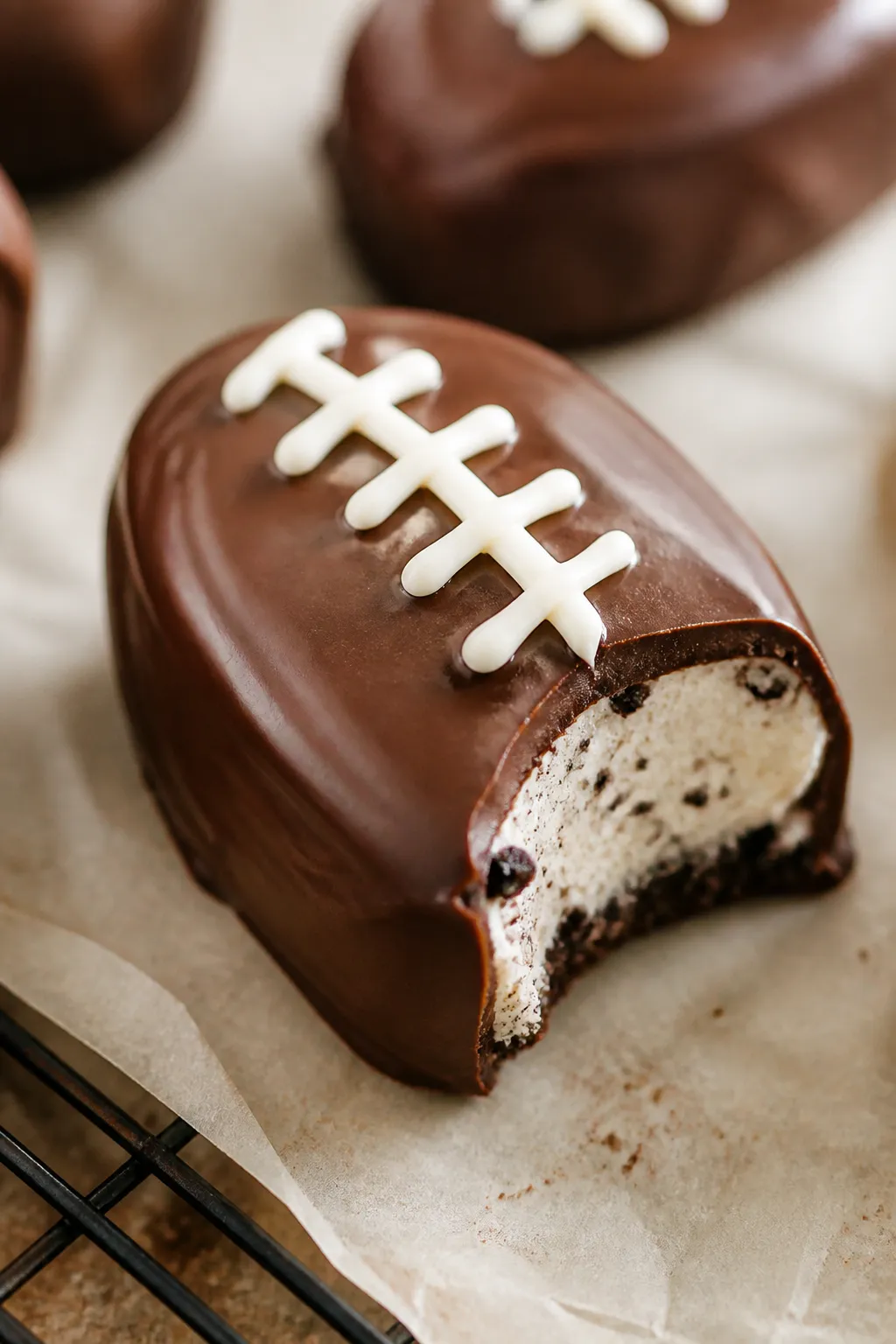 Close-up detail: A freshly dipped Football Oreo Cheesecake Bite resting on parchment, glossy semiswe