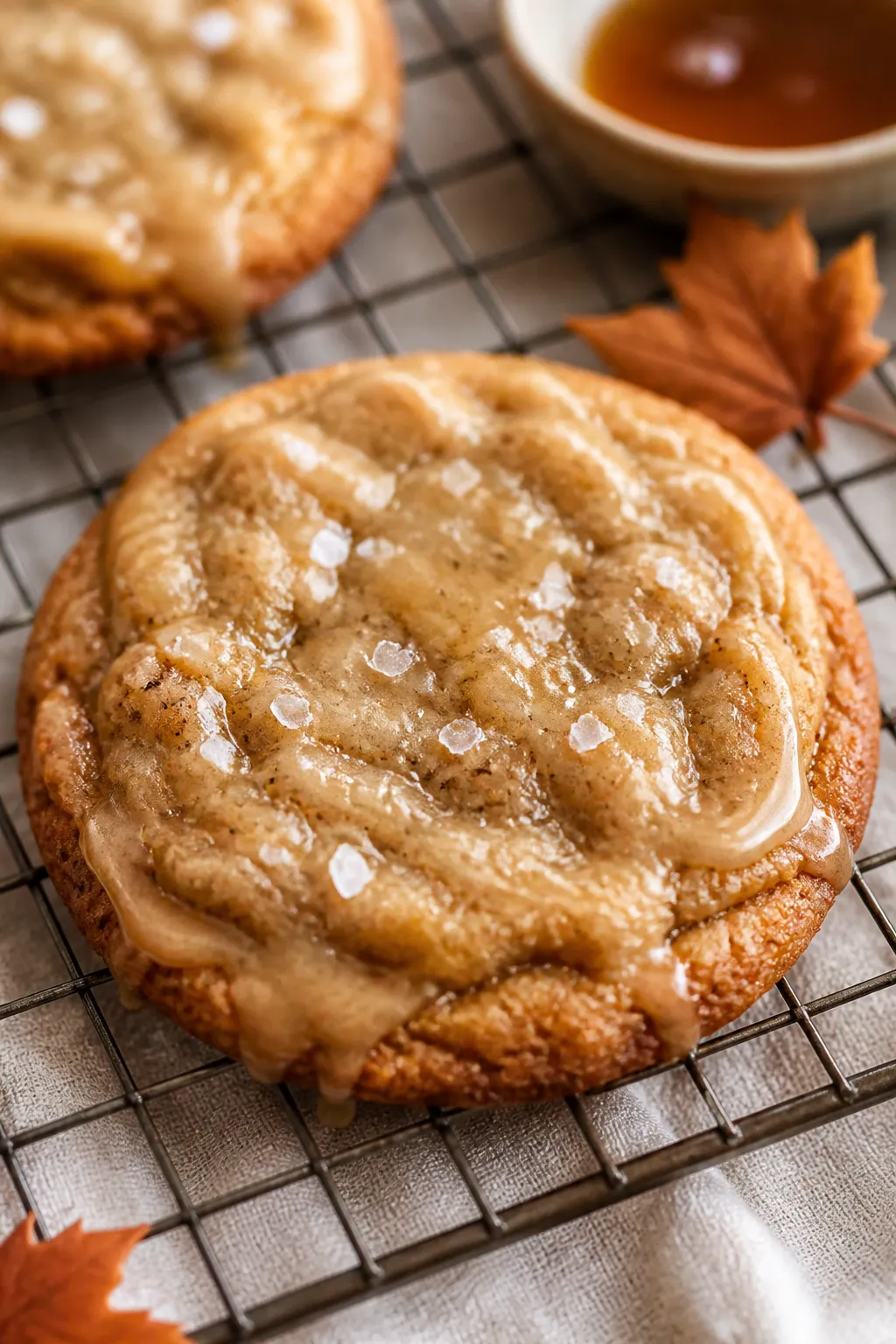 Close-up detail: A just-baked Brown Butter Maple Cookie cooling on a wire rack, edges golden and cri