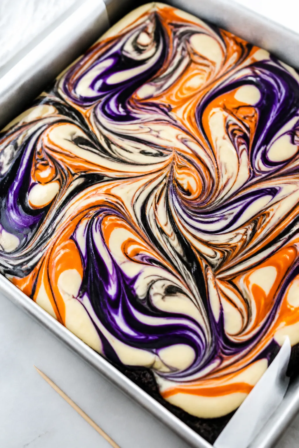 Close-up detail: A just-swirled pan of Halloween cheesecake bars before baking, overhead angle showi