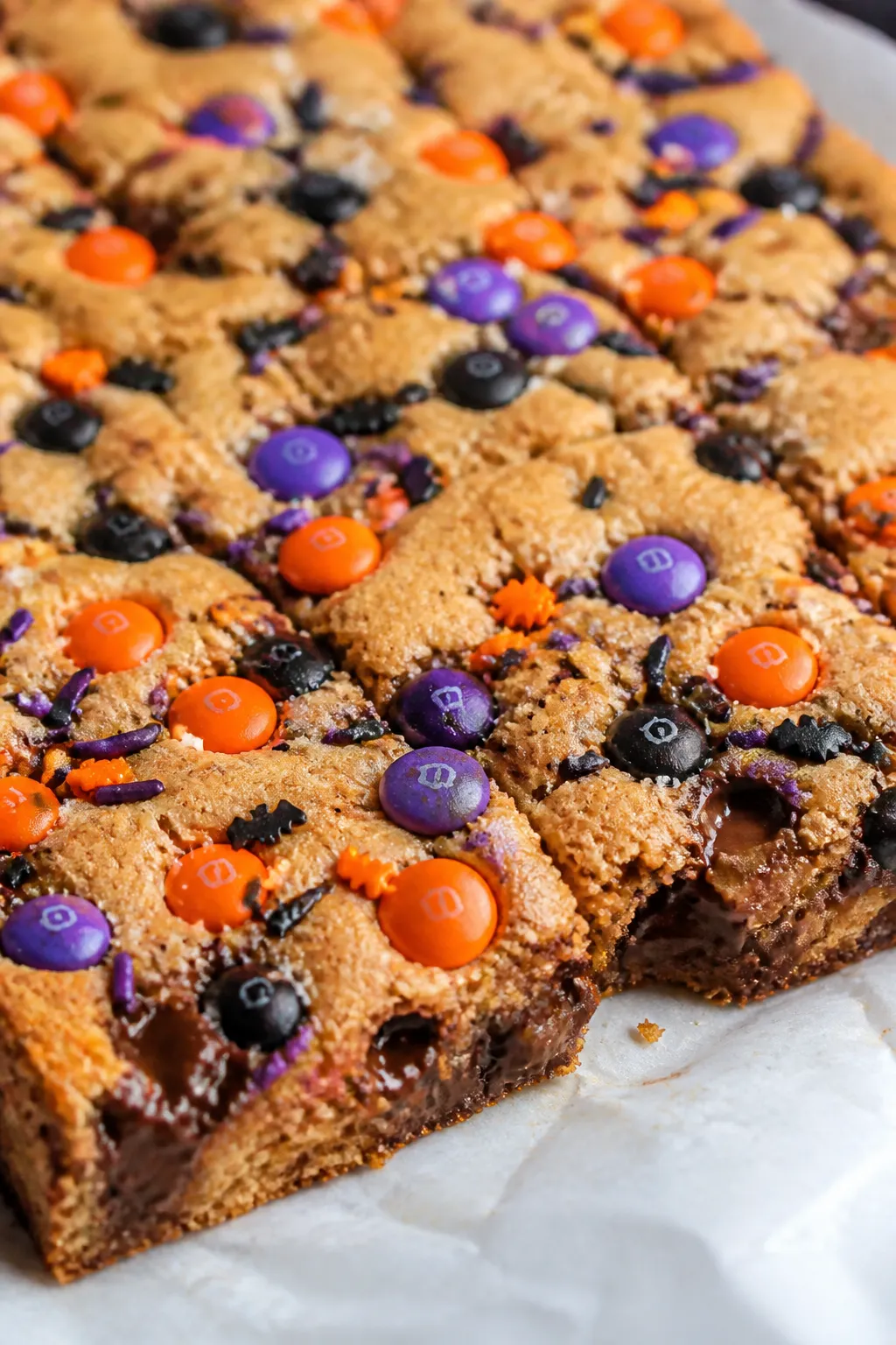 Close-up detail: Chewy Halloween M&M cookie bars just out of the oven, edges golden and center sligh