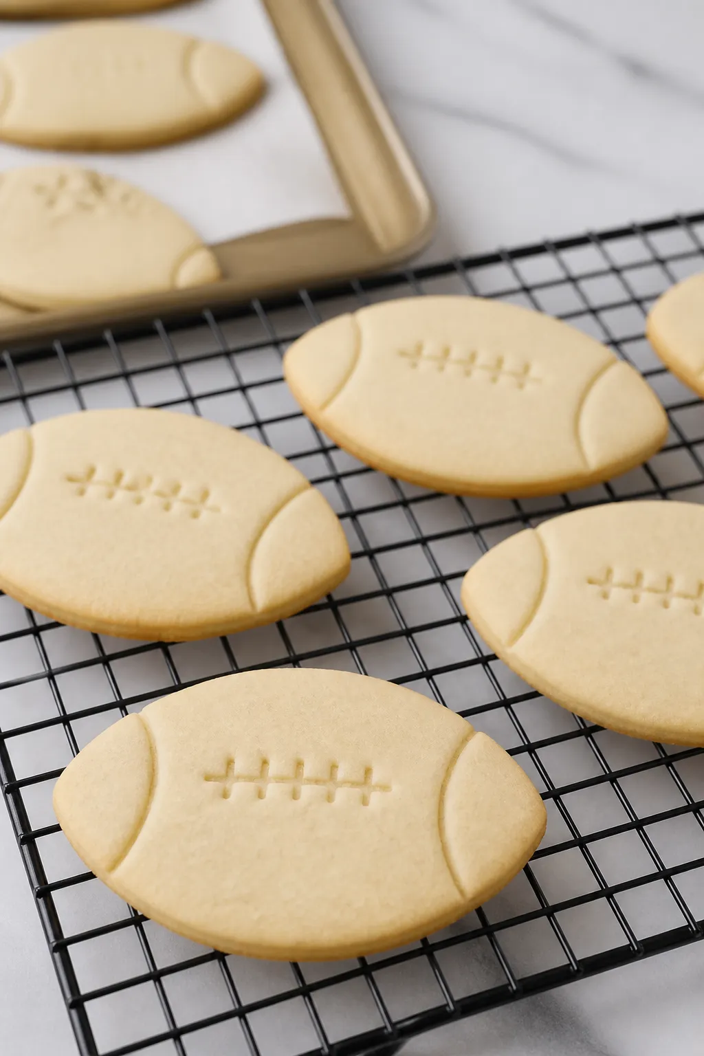 Close-up detail: Freshly baked football-shaped sugar cookies cooling on a wire rack, edges just turn