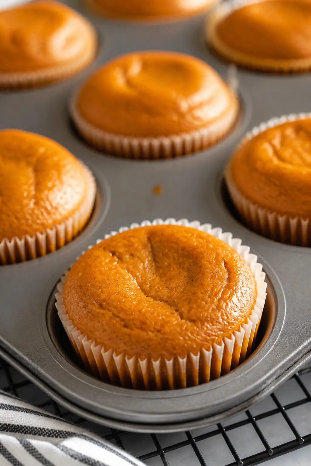 Close-up detail: Just-baked pumpkin pie cupcakes cooling in a lined muffin tin, centers gently set w