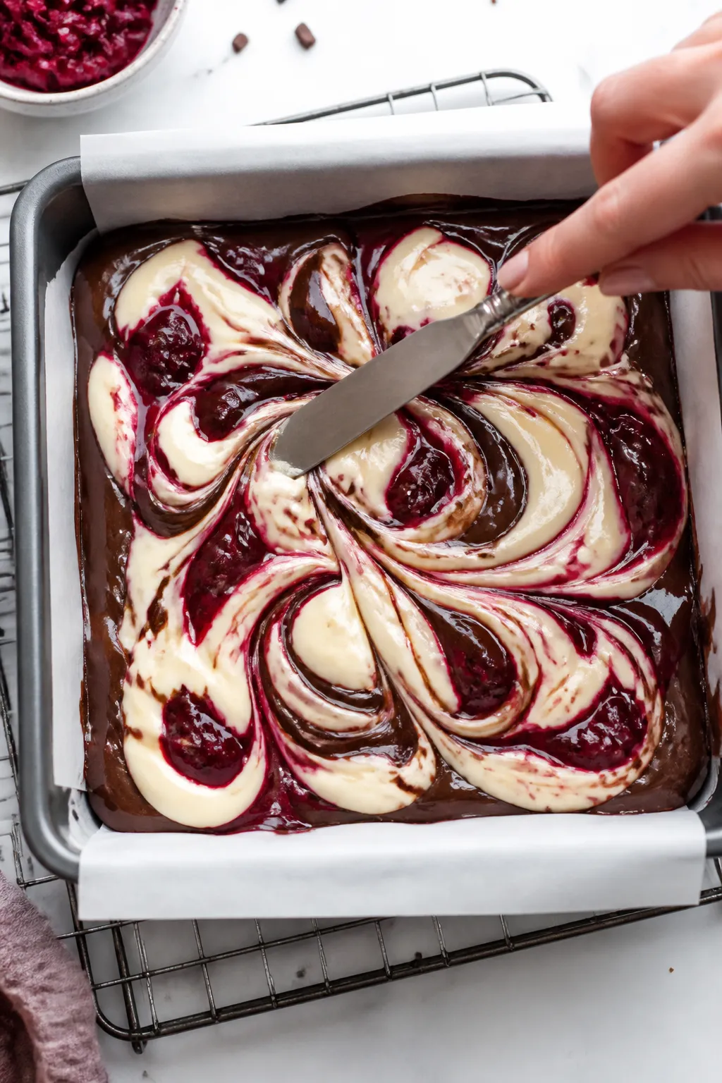 Cooking process close-up: Swirling cranberry cheesecake brownies in the pan. Overhead shot of an 8- 