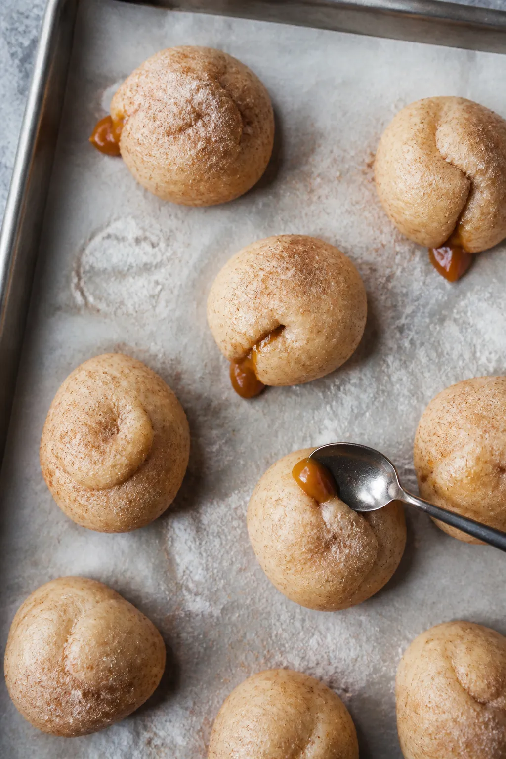 Cooking process: Overhead shot of chilled, stuffed dough balls on a parchment-lined baking tray, eac