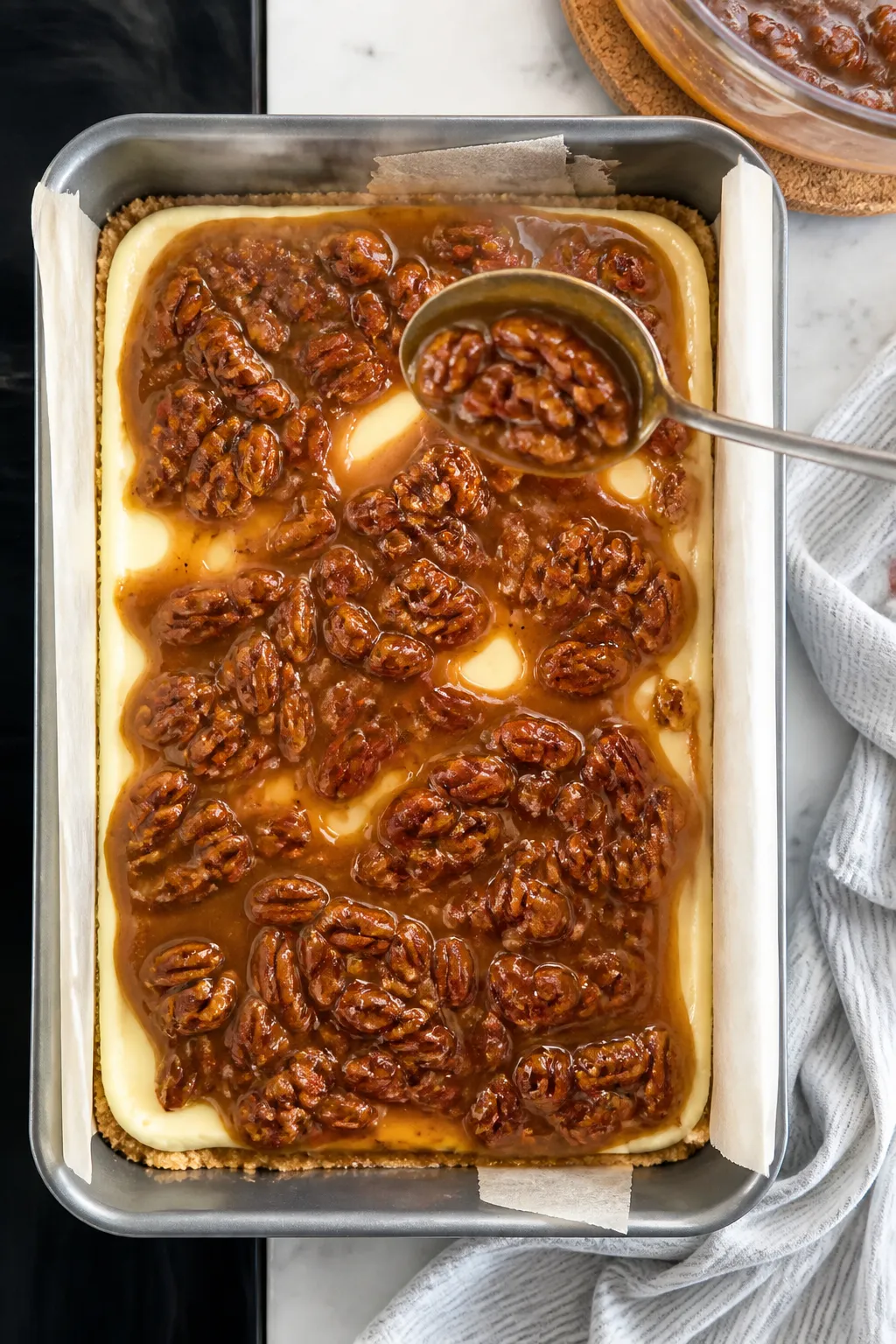 Cooking process: Overhead shot of the warm pecan topping being spooned evenly over a slightly cooled