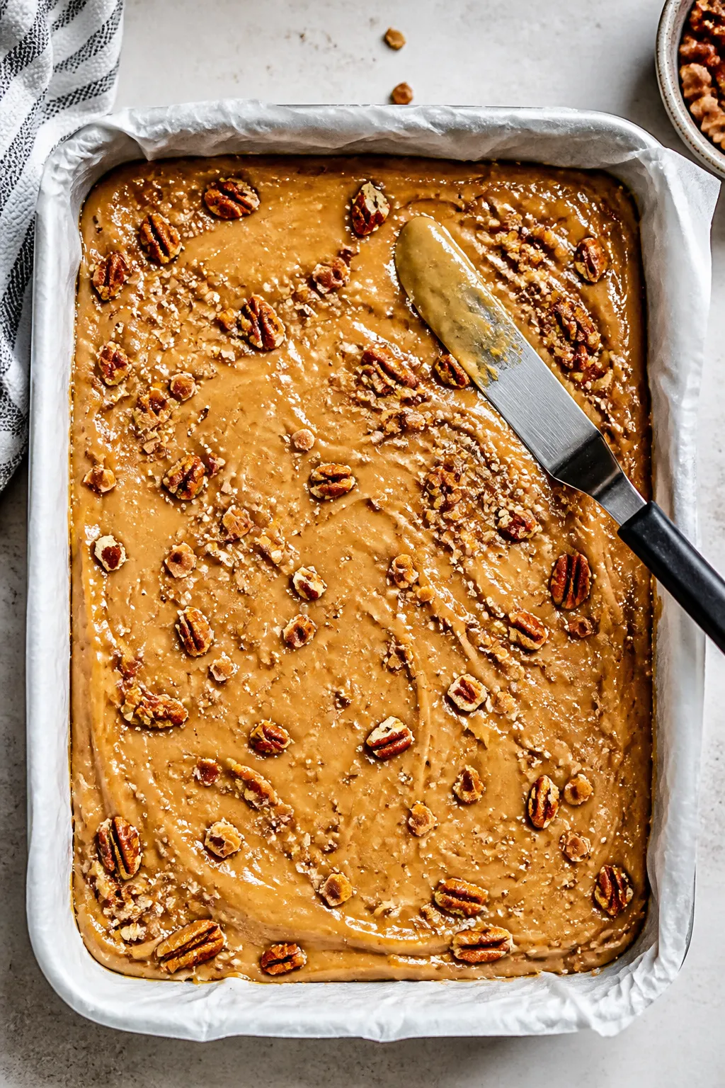 Cooking process: Thick, glossy batter being smoothed evenly in a parchment-lined pan with an offset 