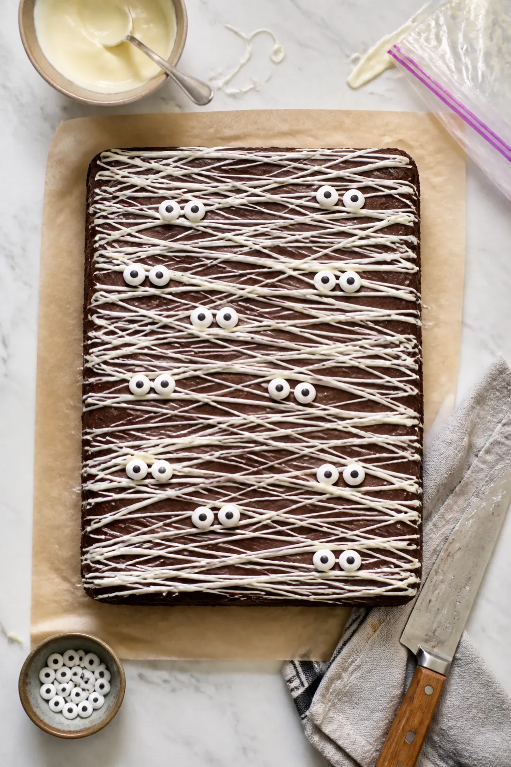 Overhead process shot of a full 9x13 slab of cooled brownies on parchment being drizzled with melted