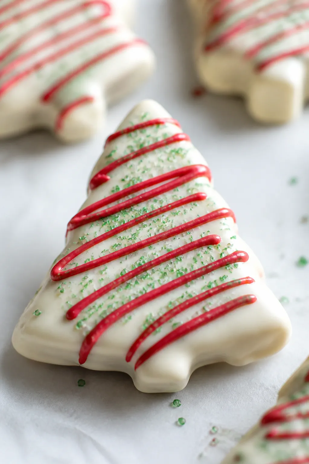 Close-up detail of a freshly coated Christmas tree sandwich cookie set on parchment, glossy white ch