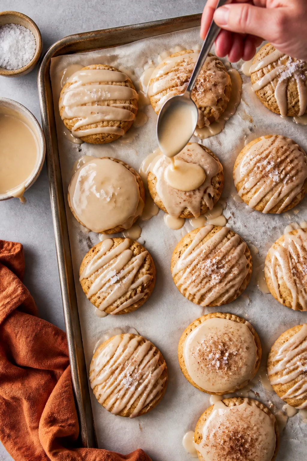 Cooking process: Overhead shot of cooled pumpkin cookies being glazed on a parchment-lined sheet pan