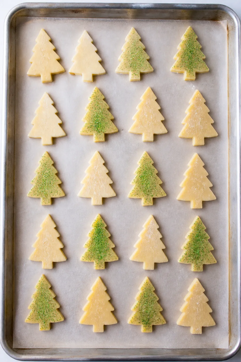 Cooking process: Overhead shot of cut Christmas tree shortbread shapes on a parchment-lined sheet pa