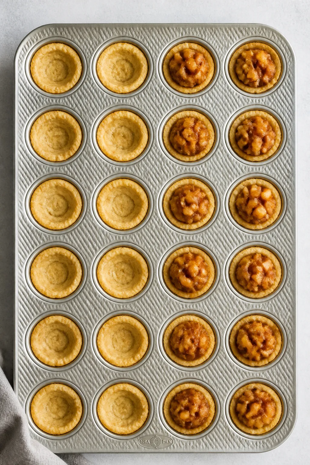 Cooking process: Overhead shot of par-baked cookie cups in a 24-cup mini muffin tin as the wells are