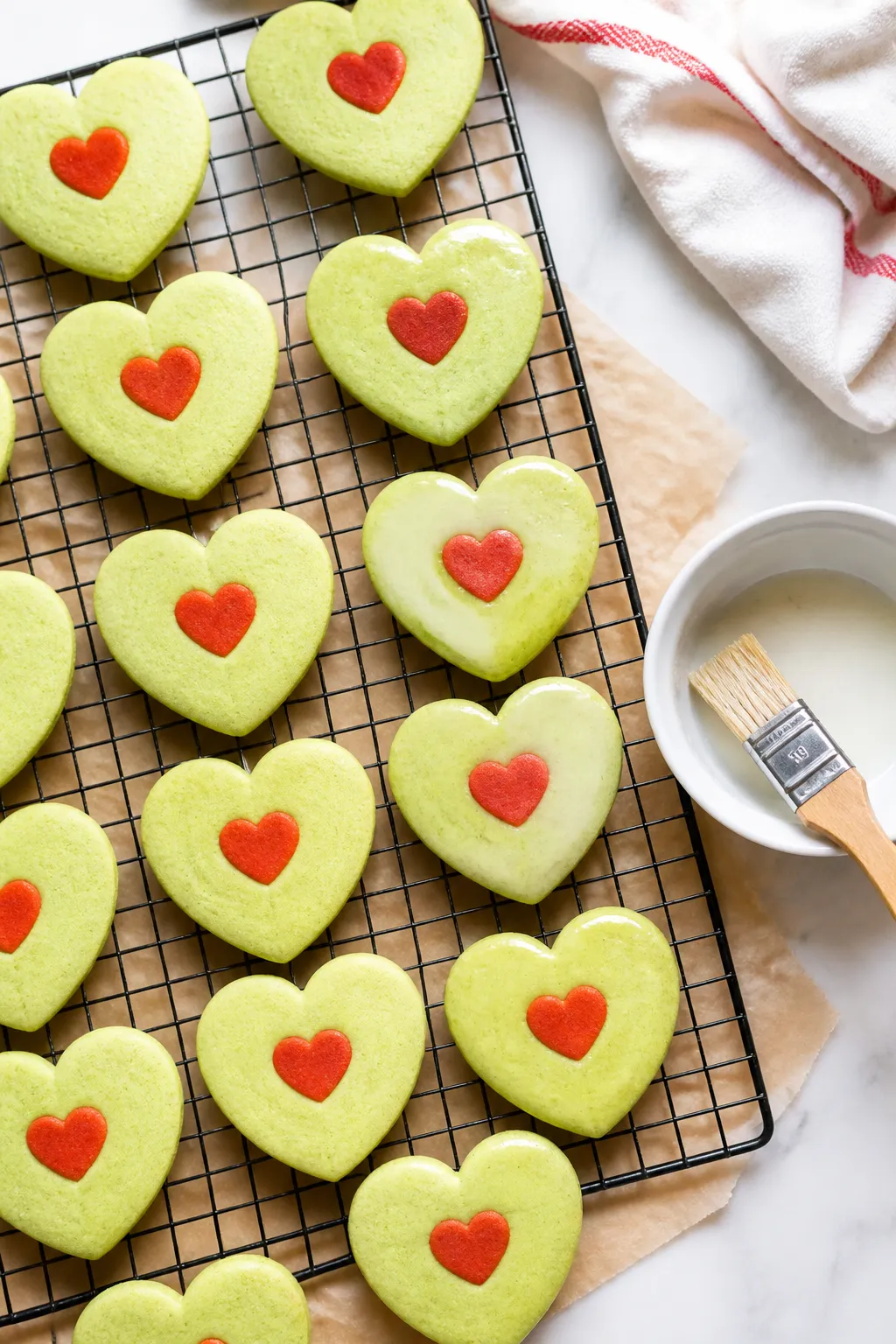Tasty top view: Overhead shot of a cooling rack filled with pale green Grinch Heart Sugar Cookies ar